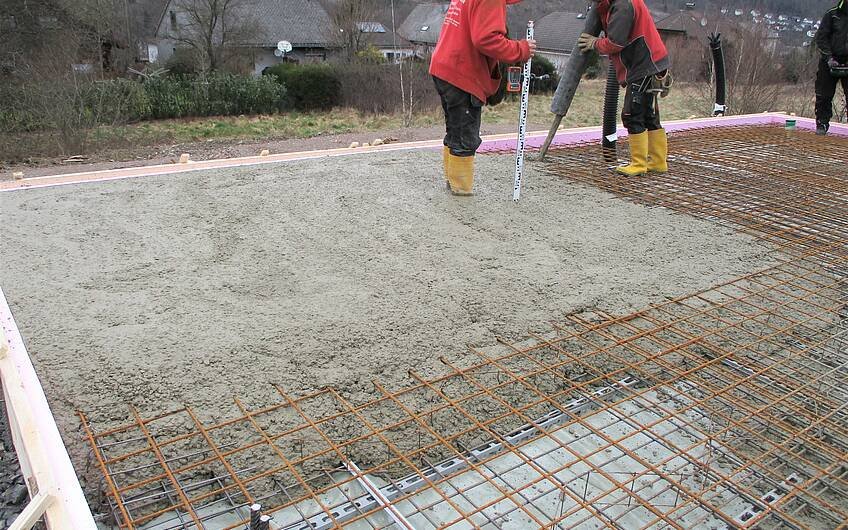 Fleißige Bauarbeiter betonieren die Bodenplatte.