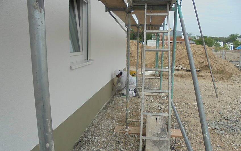 Verputzer beim Arbeiten am Sockel des individuell geplanten Einfamilienhauses Luna von Kern-Haus in Ludwigshafen