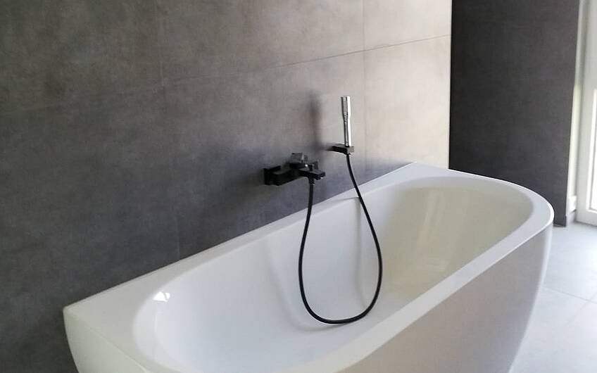 Einzigartige Badewanne an schwarzen Fliesen mit schwarzer Armatur im Bad des Kern-Haus in Halle Giebichenstein