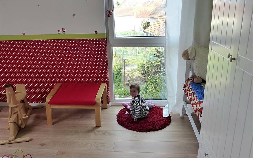 Tochter der Bauherren am Fenster ihres Kinderzimmers im Kern-Haus Komfort in Linkenheim-Hochstetten