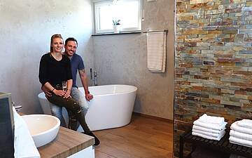 Bauherrenpaar sitzt auf Badewanne im Badezimmer der Kern-Haus-Stadtvilla Signus in Otterberg