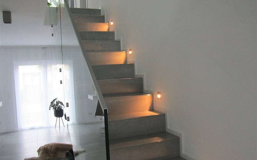 Die Treppenstufen werden elegant beleuchtet. Das Ganzglasgeländer lässt die Diele großzügig wirken.