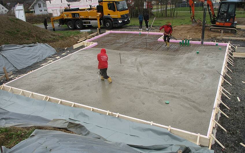 Die Bodenplatte wird von fleißigen Bauarbeitern betoniert.