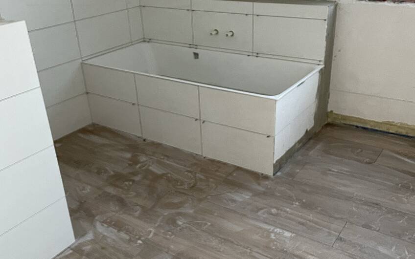 Echt schick! Die Wände des Badezimmers werden mit weißen Fliesen versehen, der Boden in moderner Holzoptik.