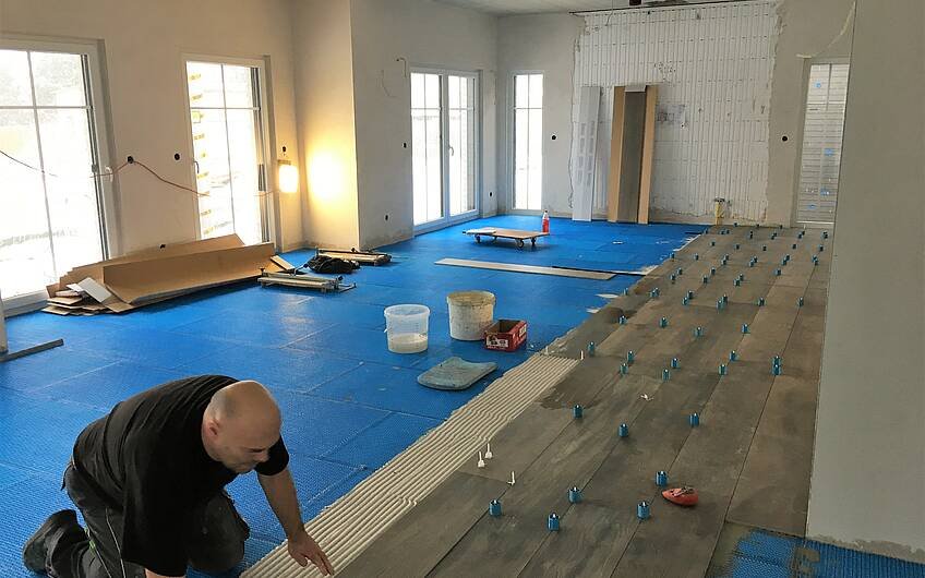 Der Fußbodenleger bringt den Bodenbelag auf die Entkopplungsmatte auf. Kern-Haus baut in Biederitz.