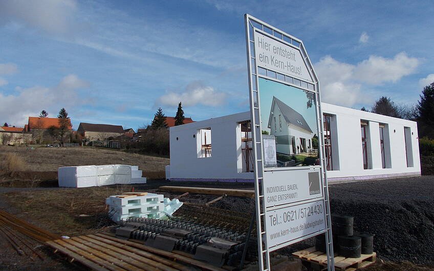 Außenansicht des Rohbau-Erdgeschosses des Familienhauses Signum von Kern-Haus in Einselthum mit Baustellenschild