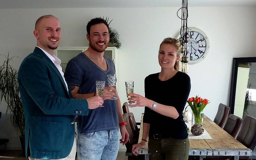 Verkaufsberater Bernd Laatz und Bauherrenpaar beim Anstoßen mit einem Glas Sekt in der Kern-Haus-Stadtvilla Signus in Otterberg