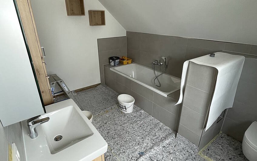Im Badezimmer trifft eine gemütliche Ausstattung auf moderne Gestaltung. Die warmen Holztöne harmonieren perfekt mit den grauen Fliesen und verwandeln diesen Raum zur wahren Wohlfühloase.