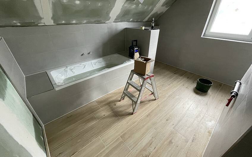 Im Bad wurde ein moderner Mix aus grauen Wandfliesen und Bodenfliesen in Holzoptik geschaffen.