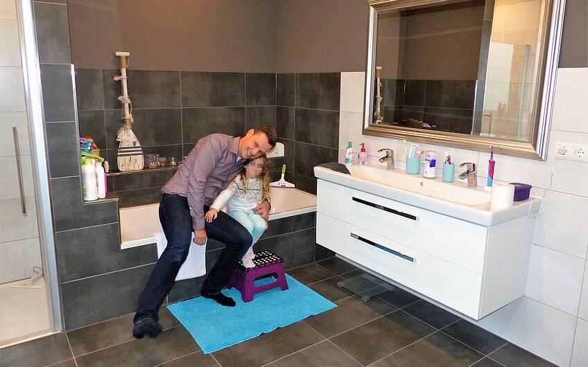 Bauherr sitzt mit Tochter auf der Badewanne im Badezimmer in der individuell geplanten Kern-Haus-Stadtvilla Signus in Dettenheim-Rußheim