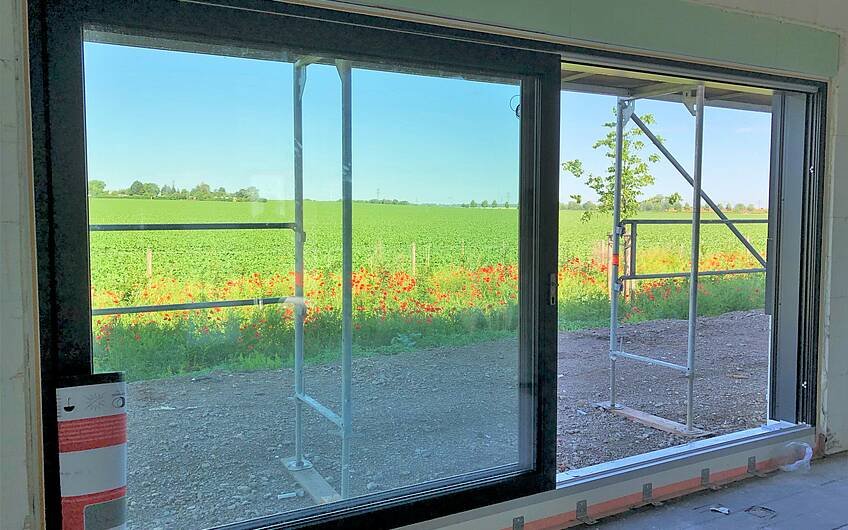 Fenster in einem Kern-Haus-Rohbau mit Sicht auf Mohnblumen