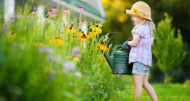 Kind gießt Blumen im Garten