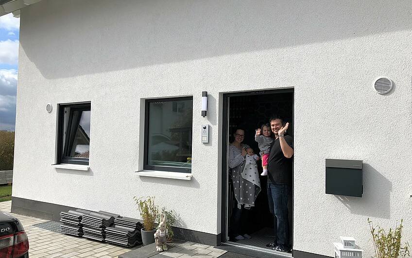 Baufamilie winkt aus der Eingangstür des individuell geplanten Einfamilienhauses Luna von Kern-Haus in Bruchsal