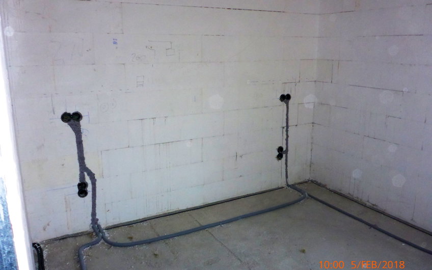 Rohbauwand mit verlegten Elektroleitungen und -dosen in der Wand.