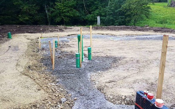 Blick auf Bauplatz mit Streifenfundament und grünen Abflussrohren.