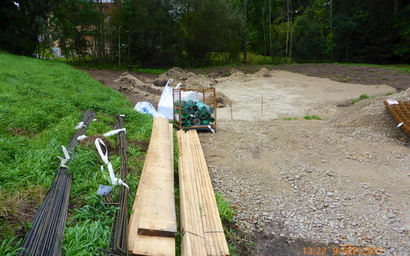 Baustelle mit gelagerten Bündeln von Stahlstäben und Holzbohlen.