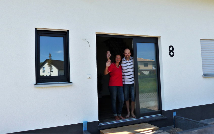 Winkende Bauherren in der Haustür des individuell geplanten Einfamilienhauses Luna von Kern-Haus in Dettenheim