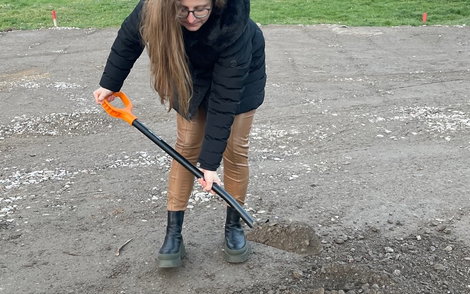 Die Bauherrin schüttet das Loch mit der Grundsteinbox zu.