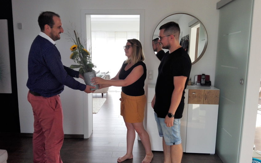 Verkaufsberater Dennis Hofmann überreicht den Bauherren des individuell geplanten Einfamilienhauses Signum von Kern-Haus in Einselthum ein Geschenk