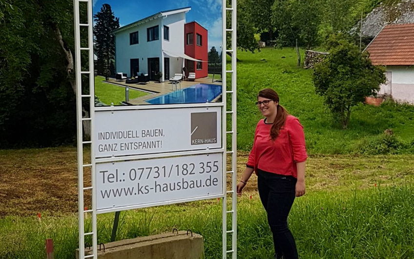 Bauherrin vor Bauschild von Kern-Haus mit Hausansicht Futura.