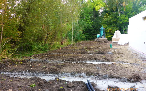Bauplatz neben dem Rohbau mit mehreren Streifenfundamenten im Boden.