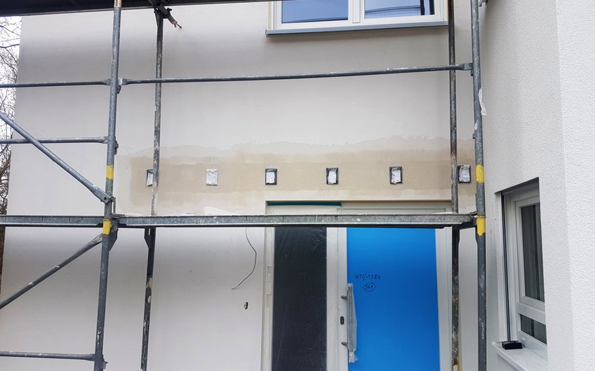 Frisch verputzte Fassade mit Metallhalterungen oberhalb der Eingangstüre.