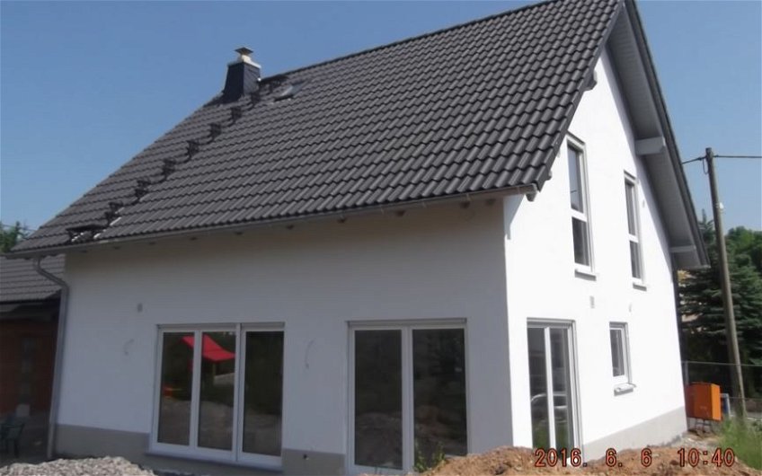 Haus mit grauem Satteldach, bodentiefen Fenstern und weißem Aussenputz