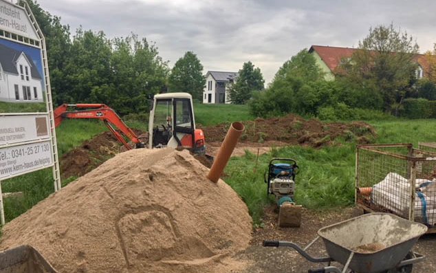 Bauschild mit Bagger und Erdhaufen vor Grundstück des Kern-Haus Baus in Wetteritz