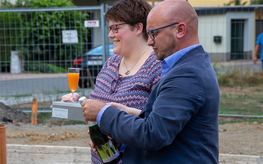 Bauherrin und Kern-Haus Verkaufsberater Ronny Hartmann beim Öffnen des Sekts für Grundsteinlegung in Eilenburg