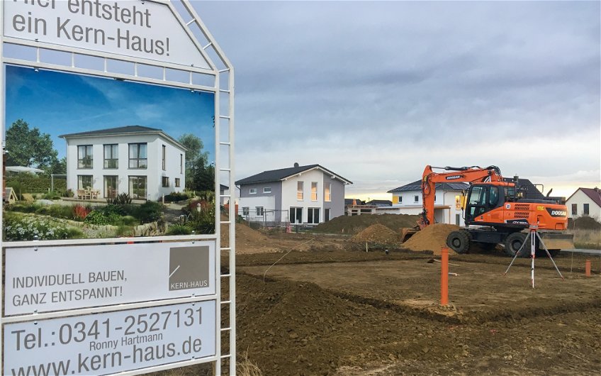 Bagger bei Herstellen des Gründungspolsters und BAuschild für Kern-HAus Stadtvilla in Kitzscher