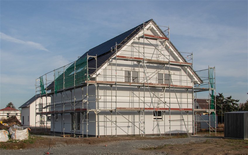 Giebelseite des Kern-Haus Familienhaus im Sonnenschein mit frischem Außenputz und Gerüst in Eilenburg