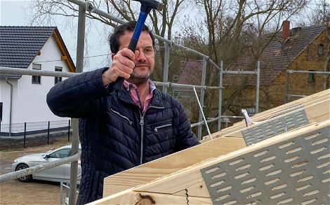 Bauherr beim Einschlagen eines langen Nagels in Dachstuhl des Kern-Haus Bungalows in Brodau