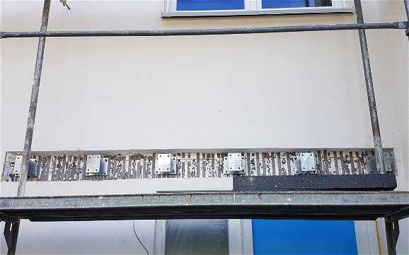 Sechs Montageprofile oberhalb der Eingangstür auf sichtbarem Betonkern der Außenwand.
