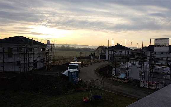 Blick auf Straße im Baugebiet mit weiteren Häusern in der Morgendämmerung.