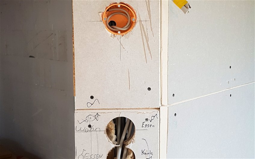Gips-Karton-Wand mit Löchern für Elektrodosen und heraushängenden Elektrokabeln.