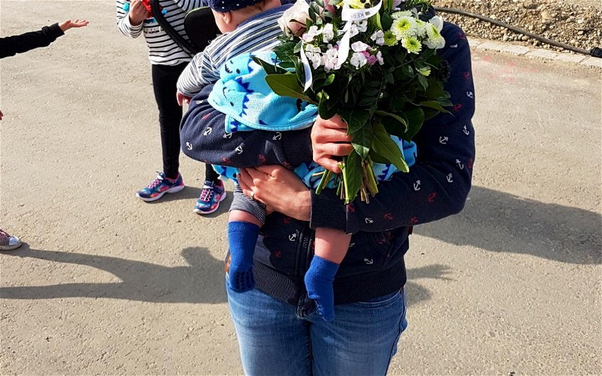 Bauherrin mit Kleinkind im Arm und Blumenstrauß in der Hand.