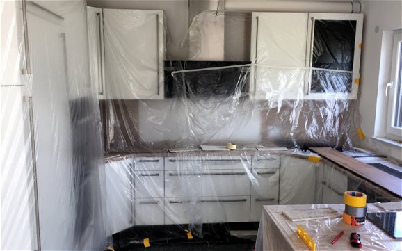 Ansicht Küche mit weißen Küchenschränken abgedeckt mit Plastikfolie.