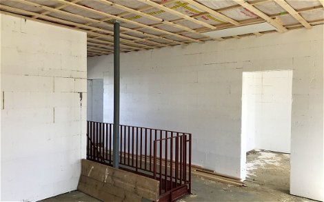 Treppenloch mit einseitig laufendem Treppengeländer und Holzbretter als Schutz auf offener Seite.