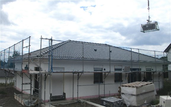 Dachmaterial wird mit Hilfe eines Kranes den Handwerkern gereicht.
